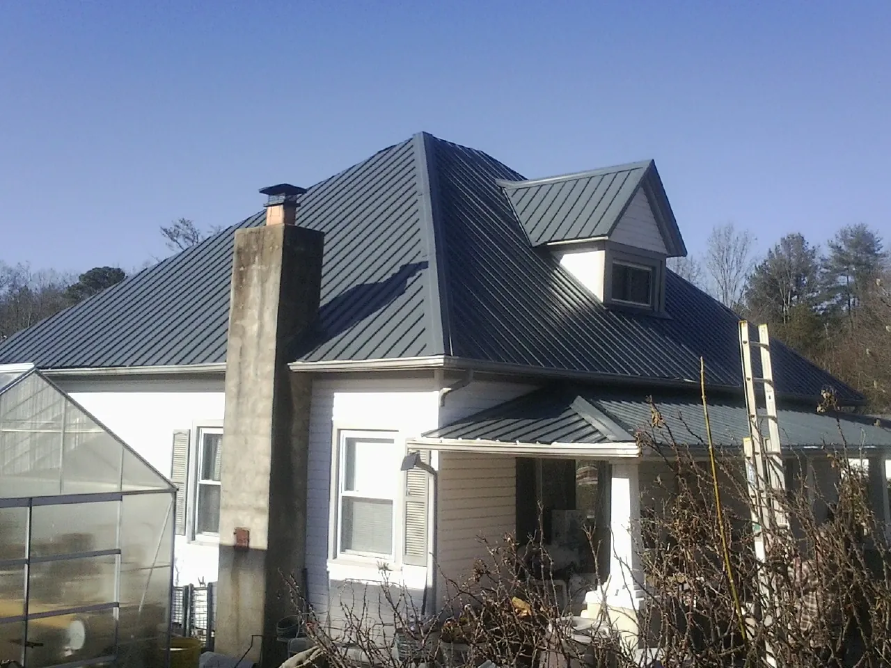 Dark blue standing seam metal roof on a white farmhouse with dormer — Slate & Tile Roof Repair by Roofing Brothers in Mc Farland