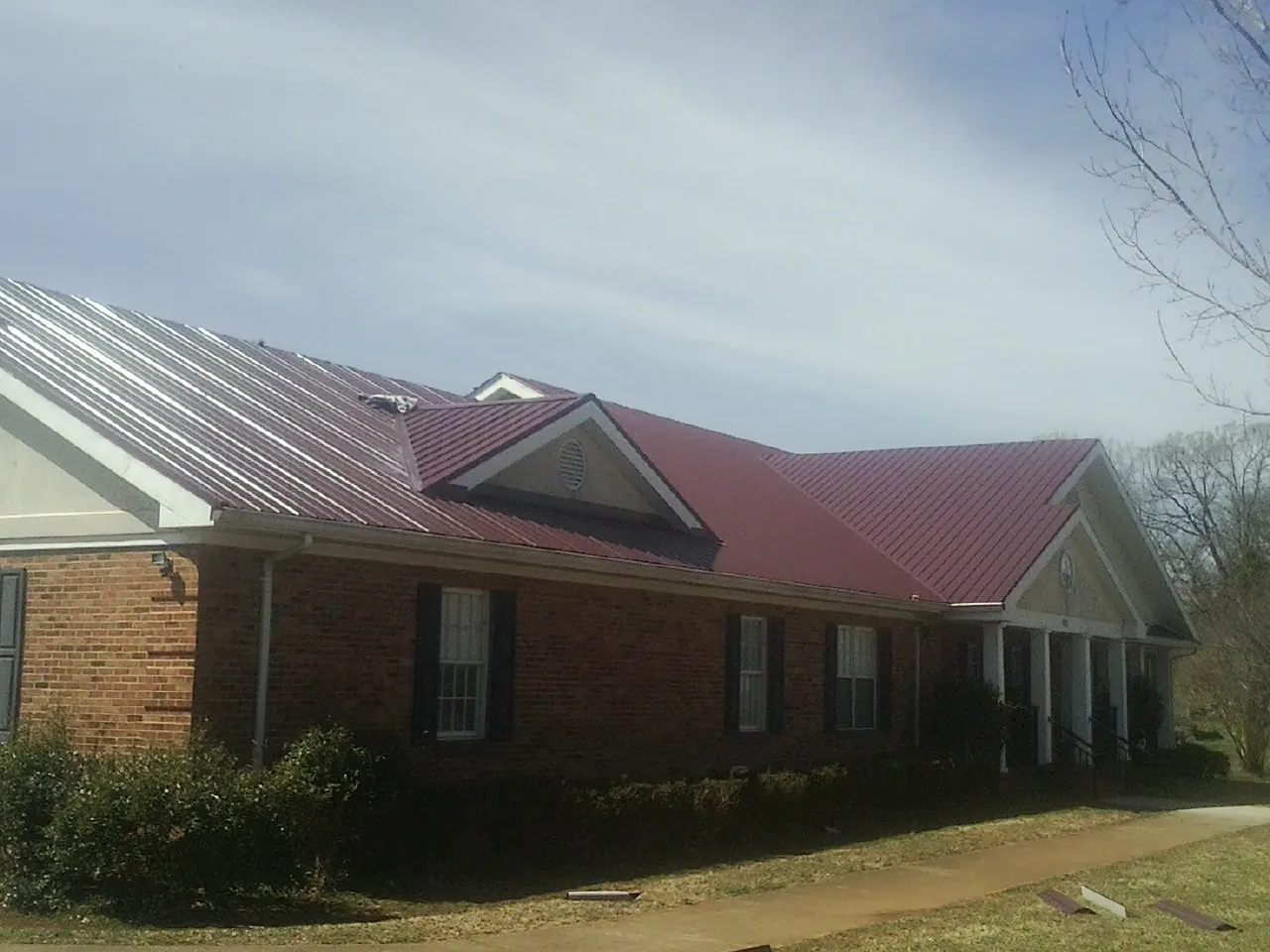 Red metal roof with gabled entries on a long brick building, from a Hail Damage Roof Repair job in Mc Farland