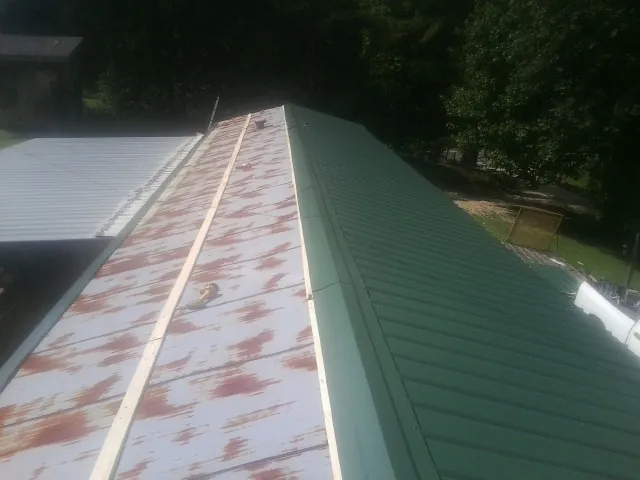 Old rusted panels beside newly installed green metal roofing — Wind Damage Roof Repair by Roofing Brothers in Mc Farland