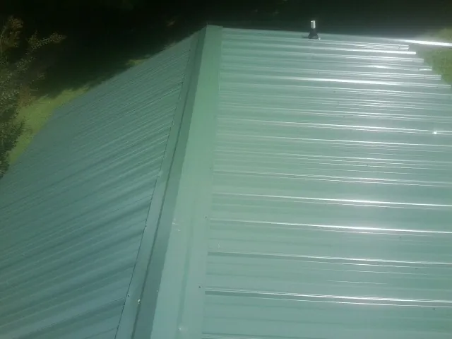 New green metal panels meeting at the ridge of a roof — Flat Roof Repair work by our crew in Mc Farland
