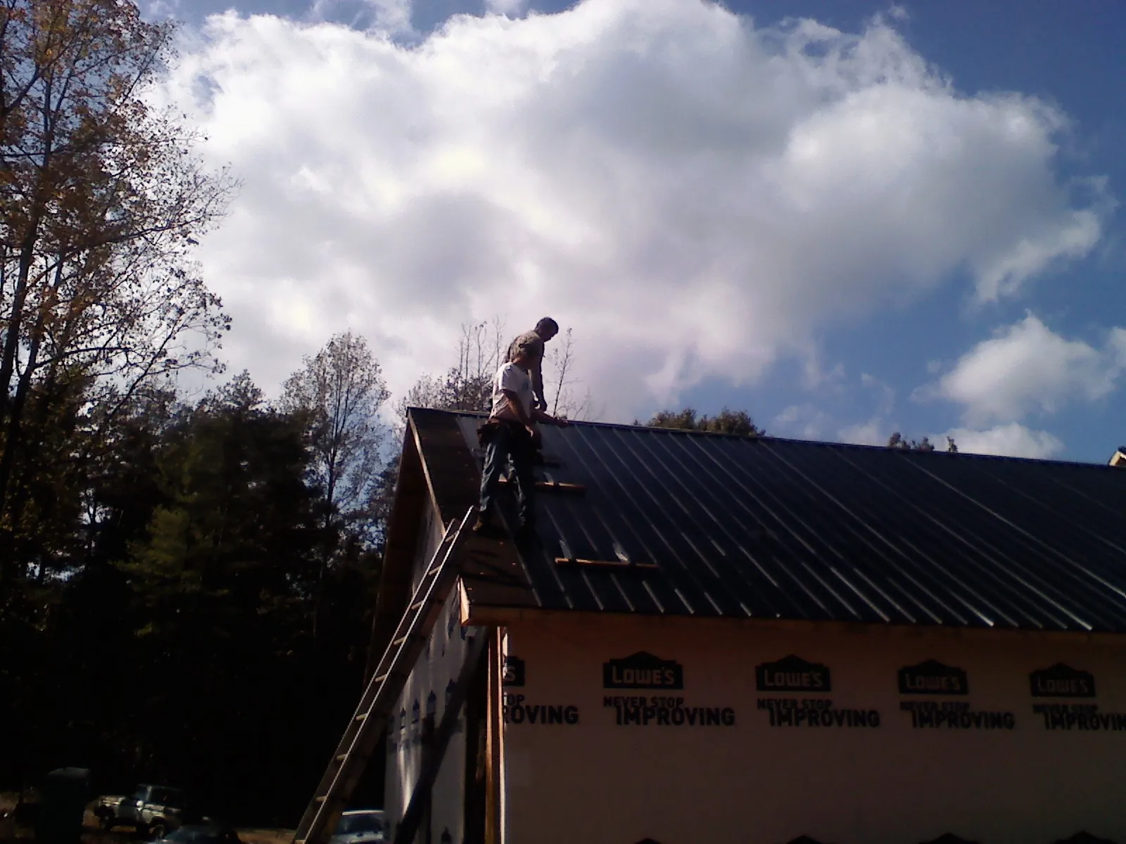 Roofer fastening dark metal panels high against a cloudy sky, from a Roof Inspection job in Mc Farland