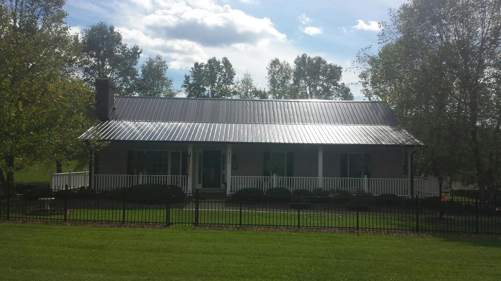 Gray metal roof on a brick ranch with a full width front porch — Gutter Guard Installation work by our crew in Mc Farland