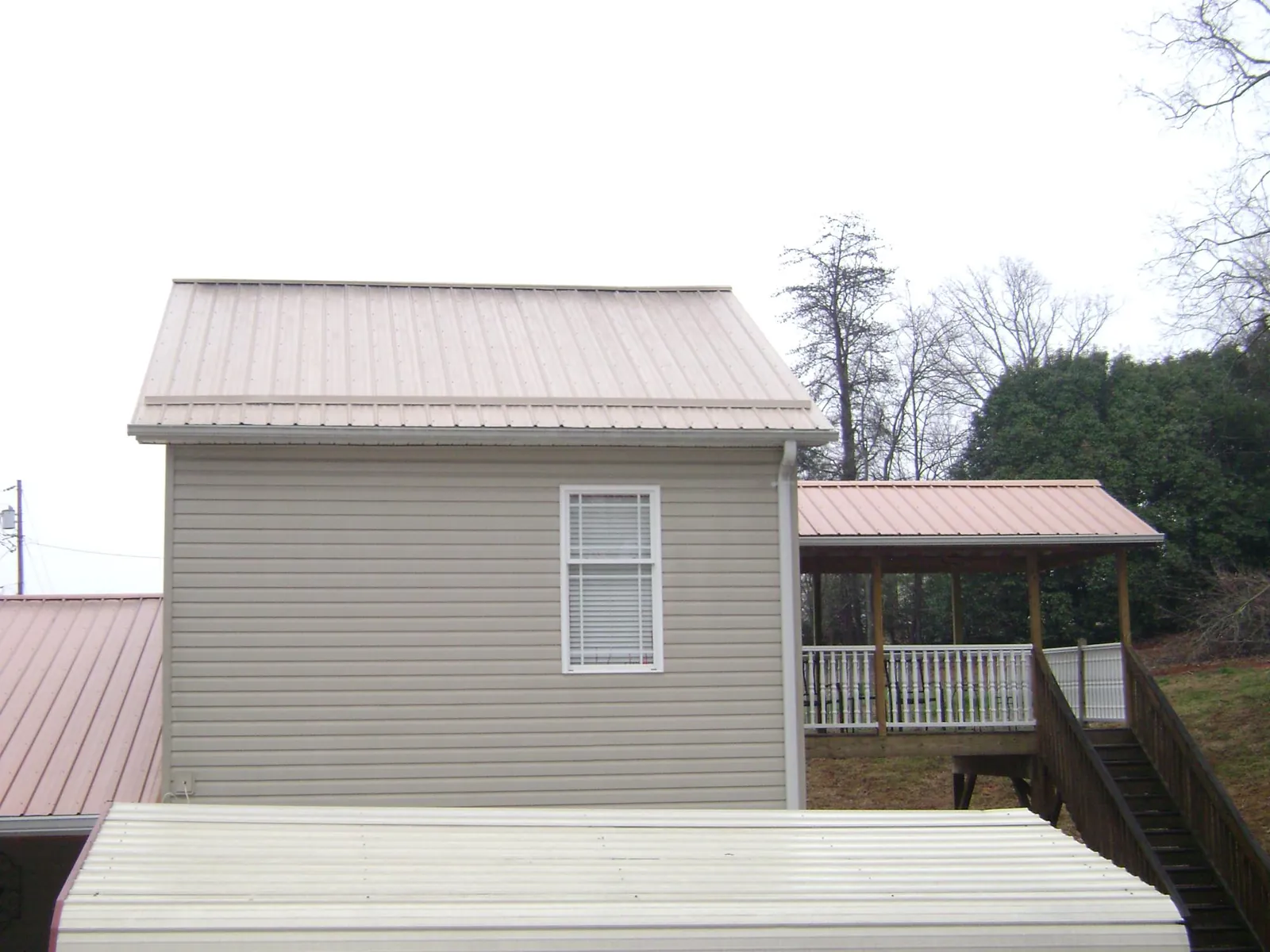 Tan metal roofs on a two story addition and attached porch, from a Roof Replacement job in Mc Farland